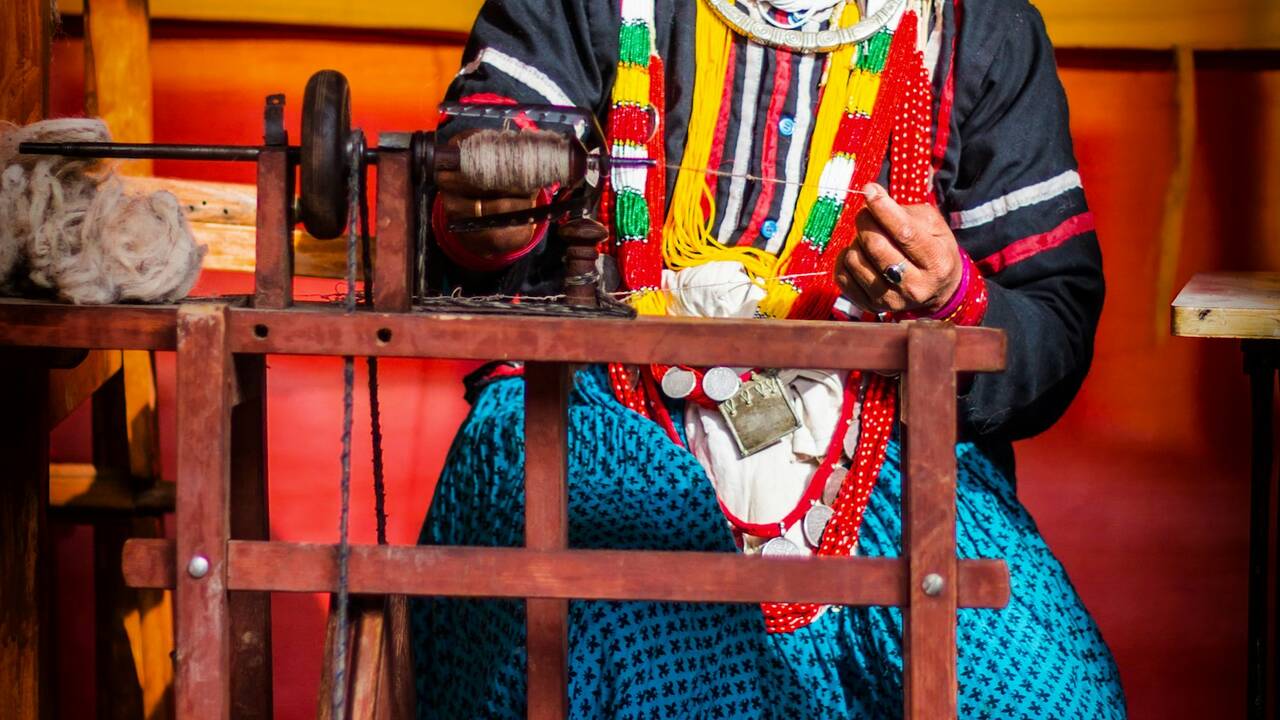 A woman in traditional dress spinning yarn on a wooden wheel
